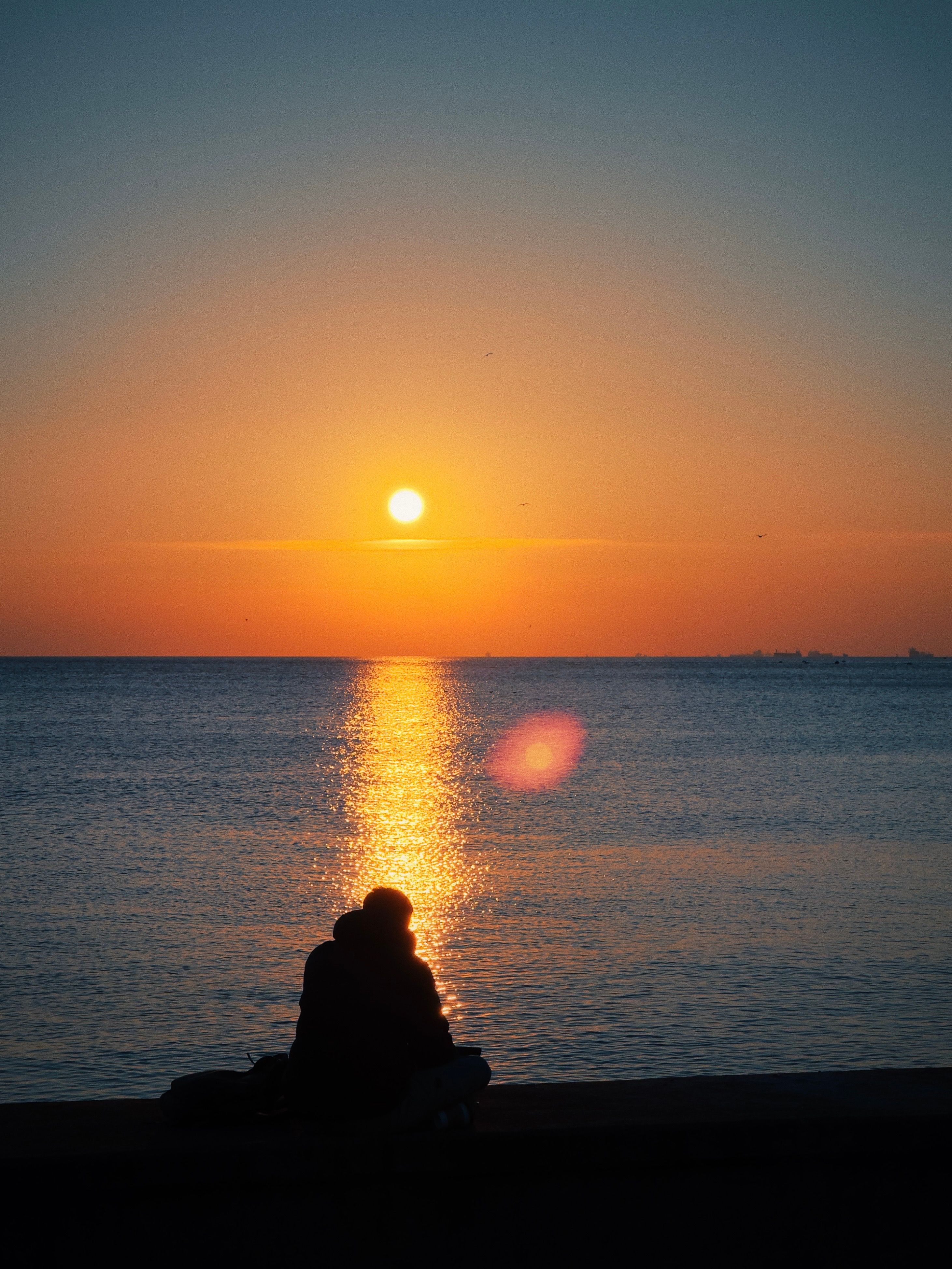 Silhouette of Person Sitting on Sea Shore at Sunset · Free Stock Photo