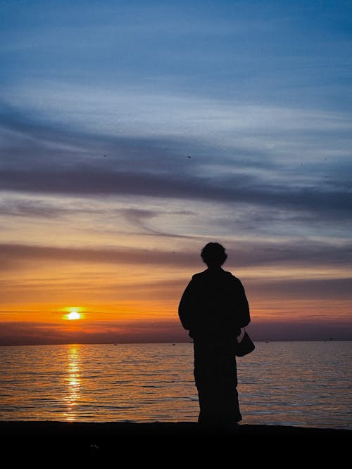 A person standing on the shore at sunset