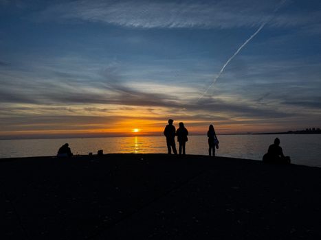 Silhouettes of people enjoying the beautiful sea view during sunset, creating a peaceful atmosphere.