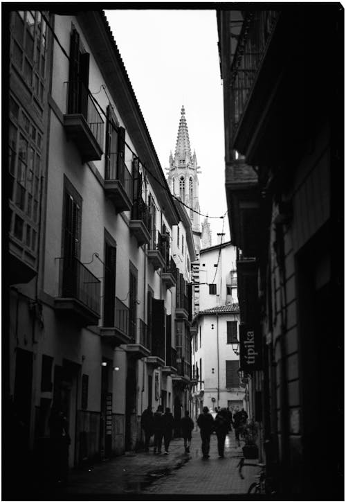 A black and white photo of people walking down a narrow street