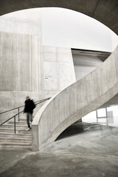 A modern architectural interior featuring a concrete spiral staircase with a blurred figure in motion.