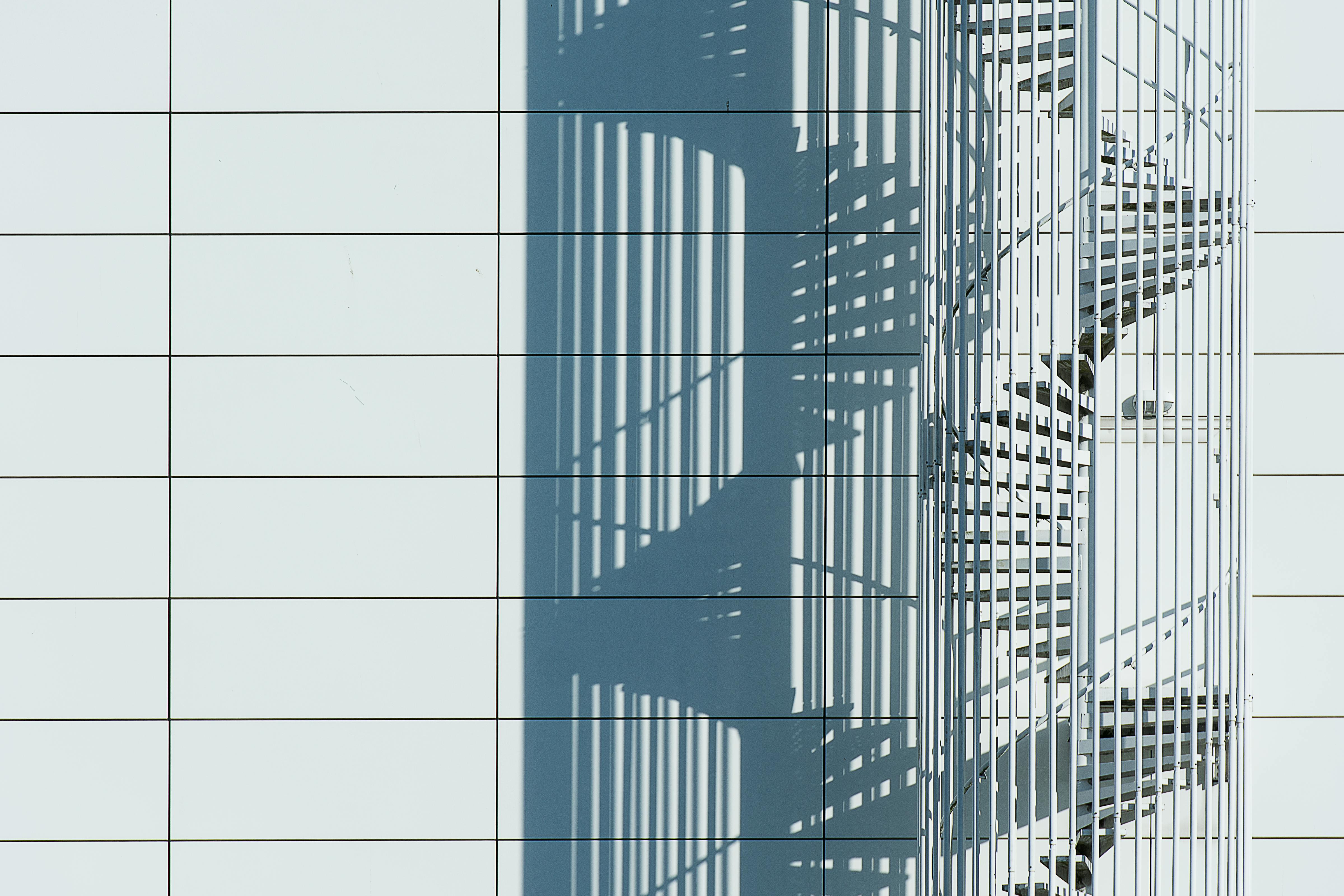 A modern spiral staircase casting geometric shadows on a white wall, emphasizing urban architecture.