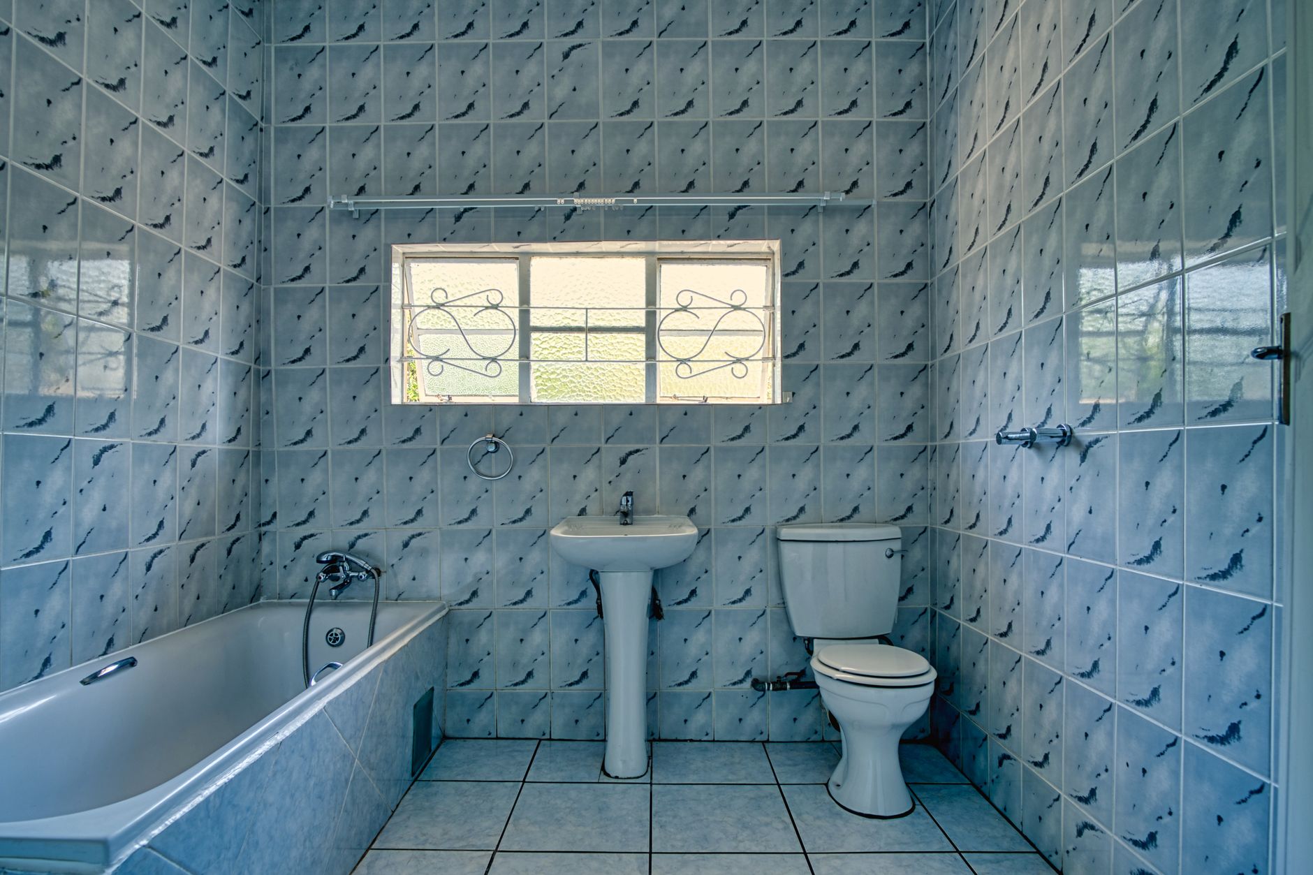 Bathroom Remodeling Trends and Tips for 2025 3 A spacious blue tiled bathroom featuring a bathtub, sink, and toilet under natural light from a window.