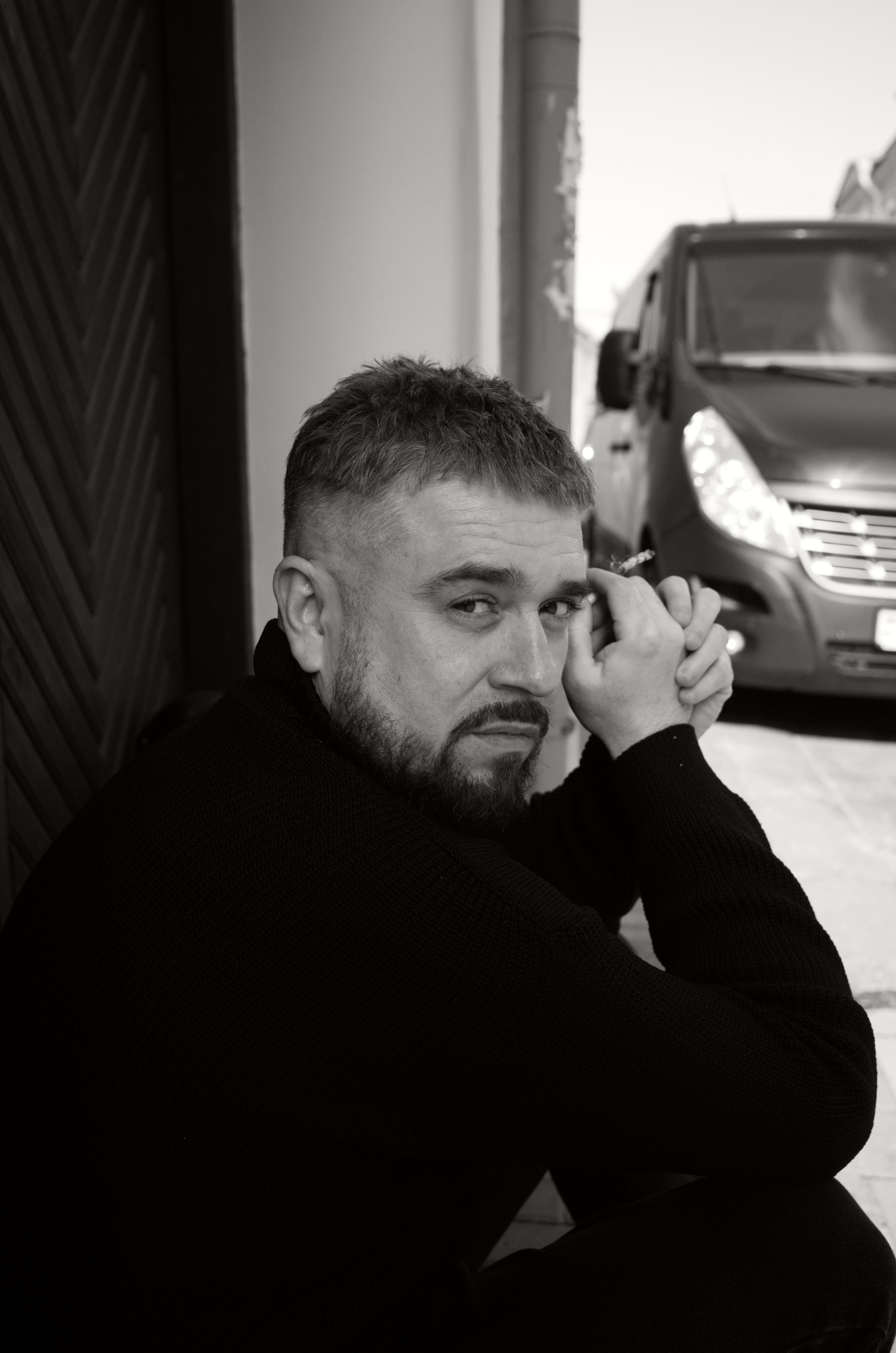 Black and white portrait of a man sitting and looking contemplatively towards the camera outdoors.