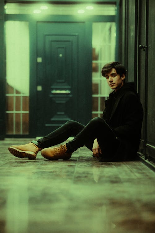 A young man sitting on the floor in front of a door
