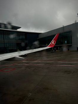 View of an airplane wing at Istanbul Airport on a rainy day, capturing urban travel vibes.