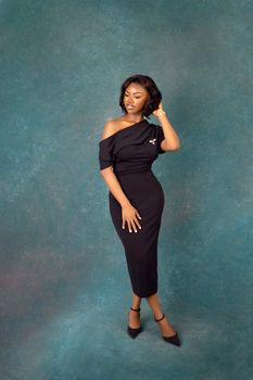 A woman in a stylish black bodycon dress poses elegantly in a studio setting.