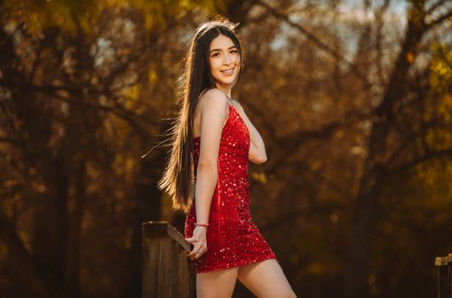Free Smiling woman in a bright red dress standing by a wooden railing under the sun. Stock Photo