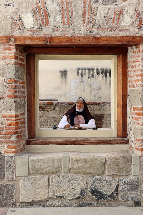 A nun looking out of a window in a brick building