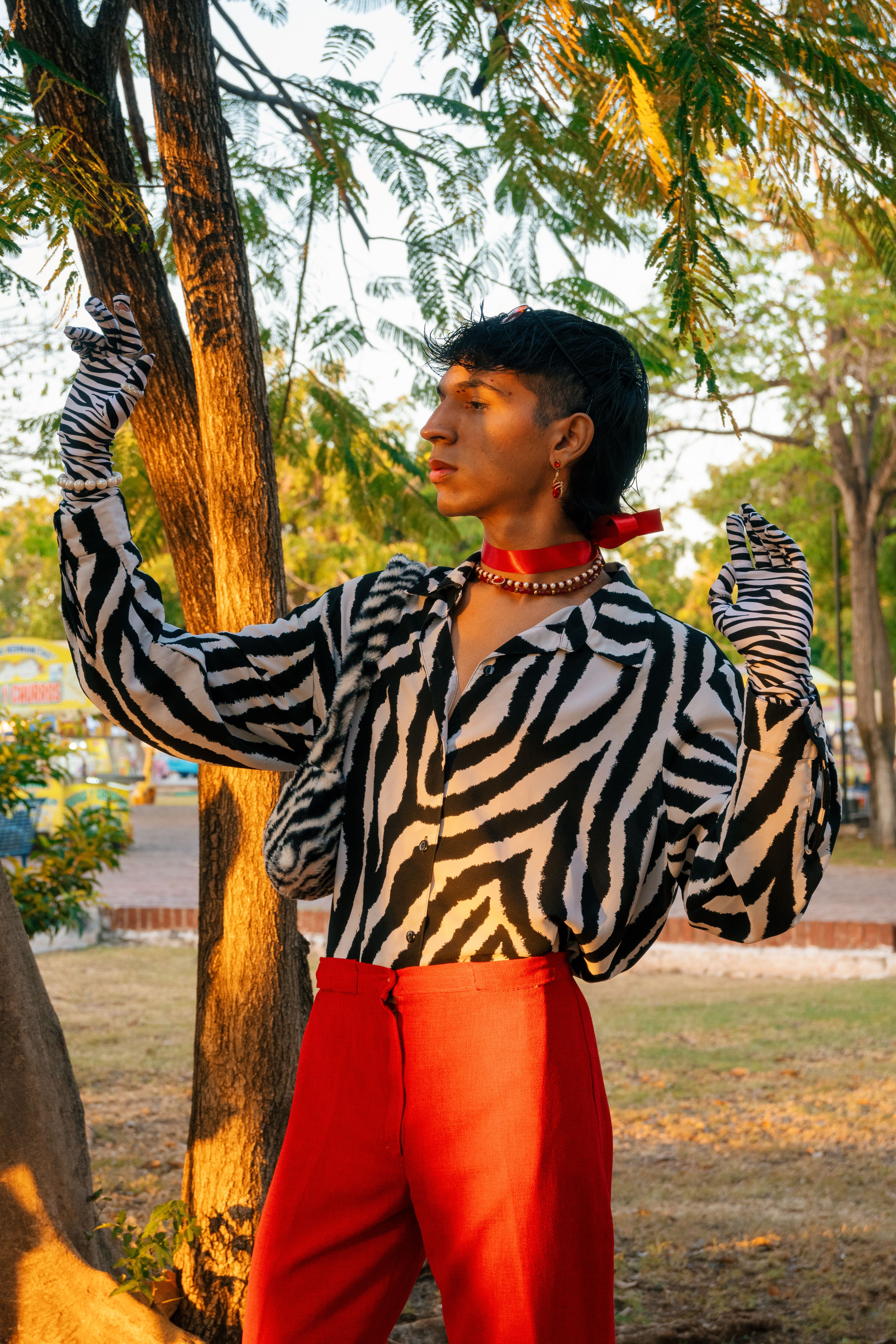 A fashion model in vibrant clothing poses confidently outdoors in a sunlit park.