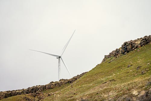 A wind turbine on a hillside with a cloudy sky