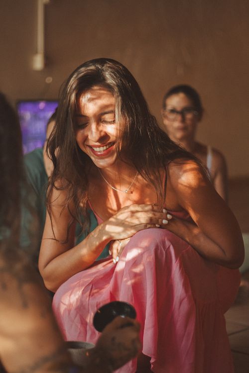 Free Smiling woman in a pink dress crouching indoors, enjoying laughter with friends. Stock Photo