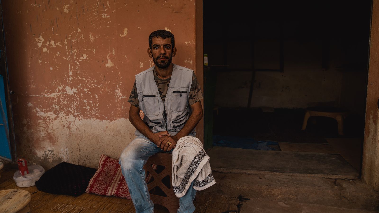 Man in vest and jeans sitting in house doorway, Morocco
