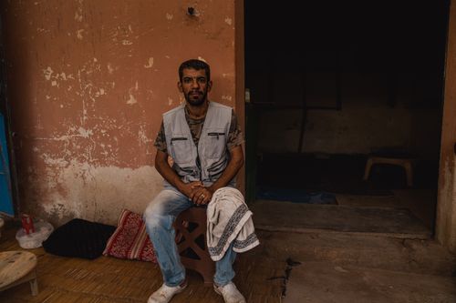 Free A man with a short haircut sits in a Moroccan village wearing a vest and jeans. Stock Photo