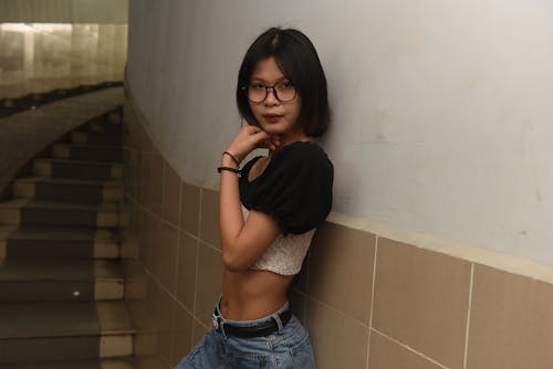 A woman in jeans and a top leaning against a wall