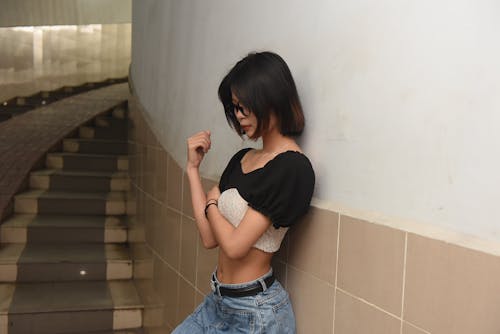 A woman in jeans and a top leaning against a wall