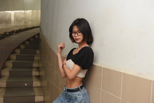 A woman in jeans and a top leaning against a wall