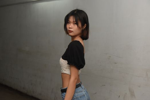 Portrait of an Asian woman with short hair standing against an urban wall.