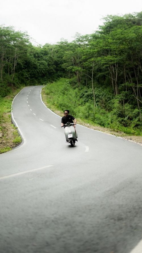 Free A person riding a motor scooter on a winding forest road surrounded by lush greenery. Stock Photo