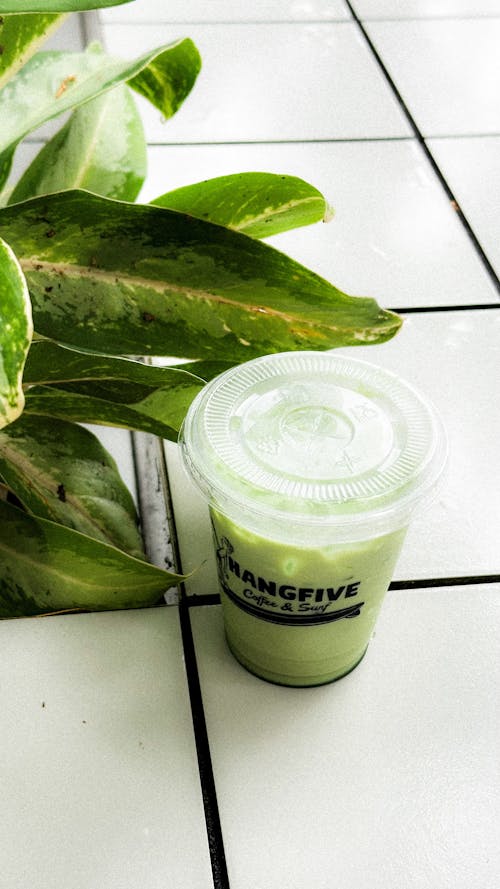 A green smoothie sitting on a tiled floor next to a plant