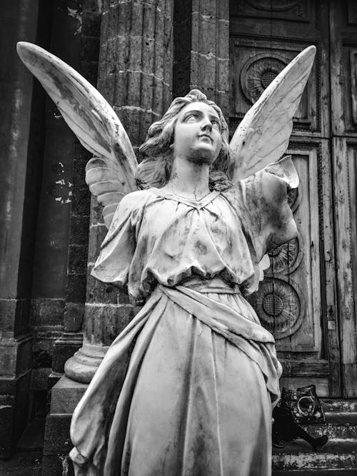 Black and White Photo of an Angel Statue on the Background of an Old Church 