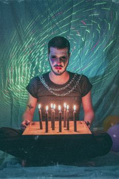 A spooky clown with smudged makeup sitting with lit candles, creating an eerie atmosphere.