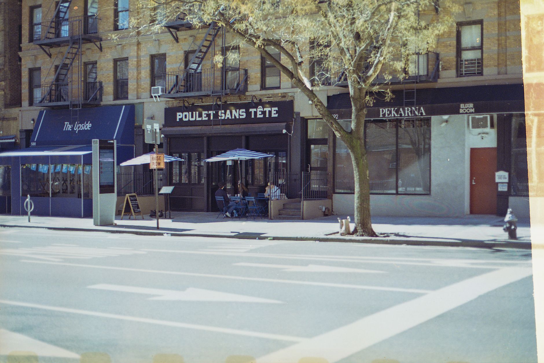 A sunny day street view of restaurants on Amsterdam Avenue, NYC, featuring outdoor seating.