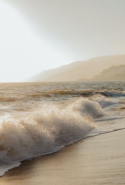 Serene sunset over the ocean with gentle waves crashing on a sandy beach.