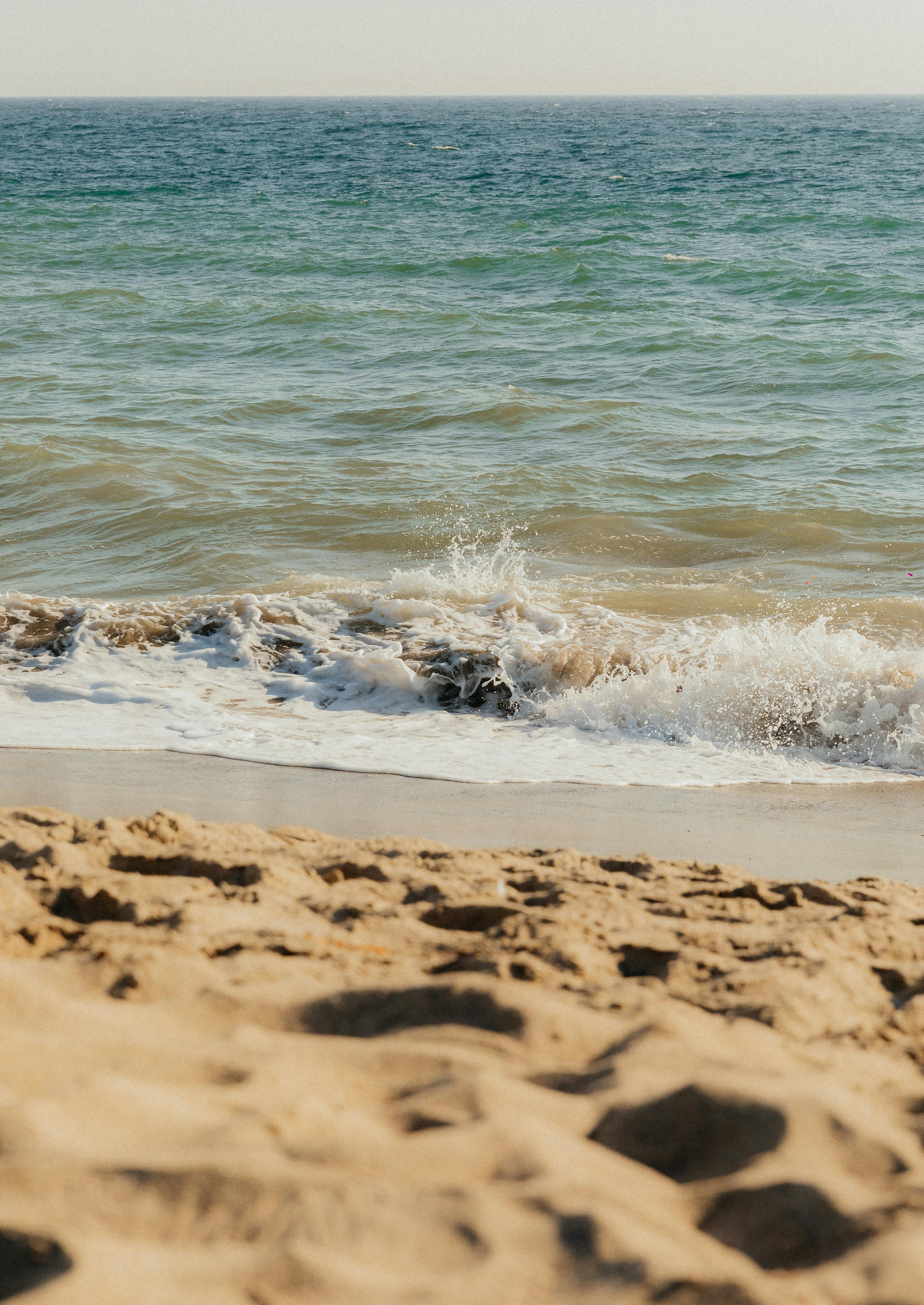 Peaceful sandy beach with gentle ocean waves under a clear sky.