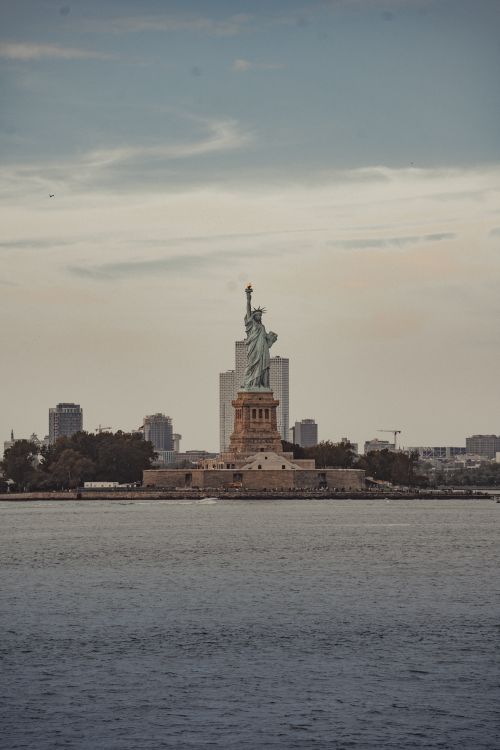 Free Distant view of the Statue of Liberty surrounded by cityscape and calm waters. Stock Photo