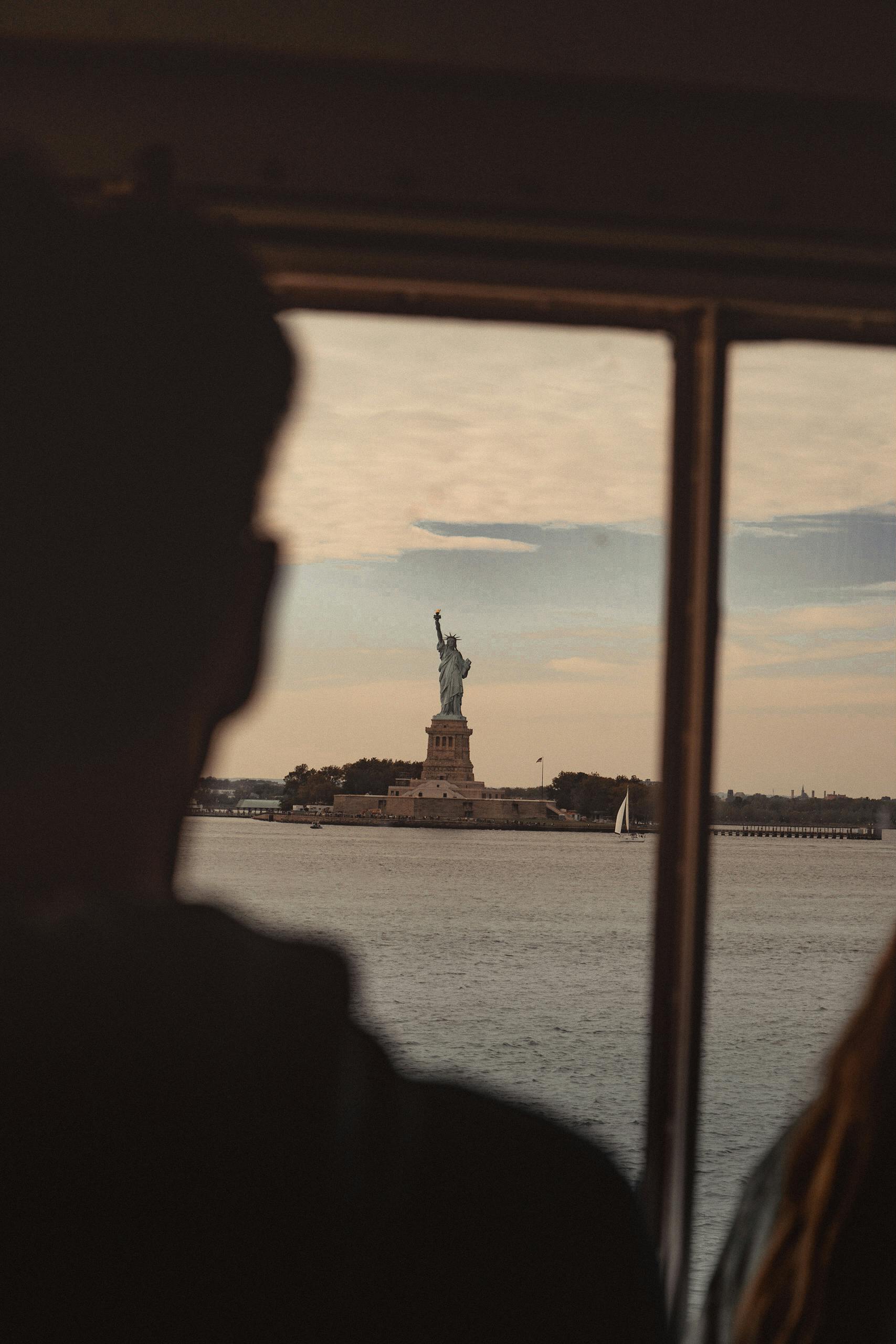 Silhouette view of Statue of Liberty from ferry window during a beautiful sunset in New York City.