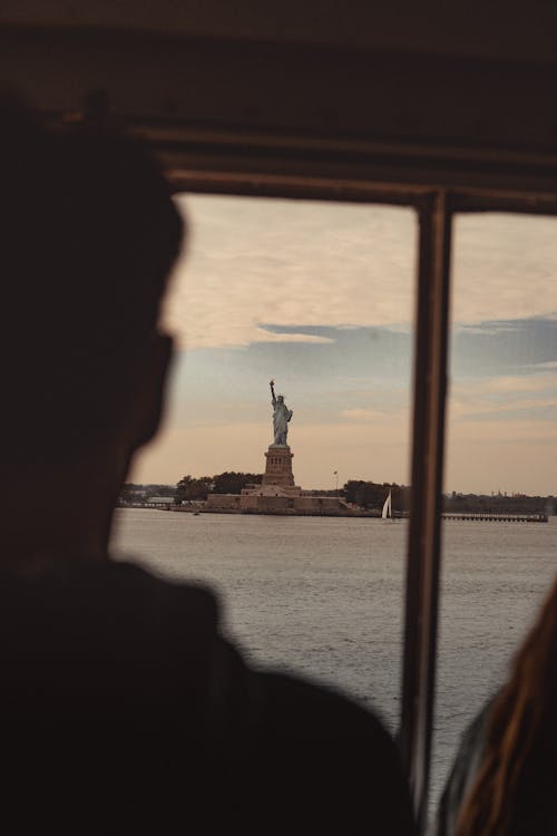 A man and woman looking out of a window at the statue of liberty