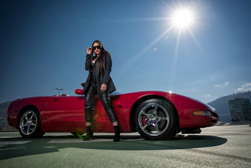 A woman standing next to a red sports car