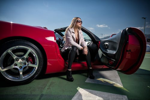 A woman sitting in front of a red sports car