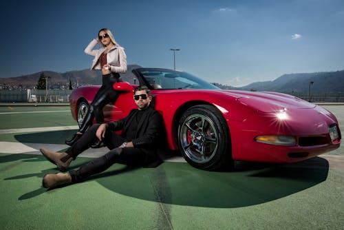 A man and woman sitting on the hood of a red sports car
