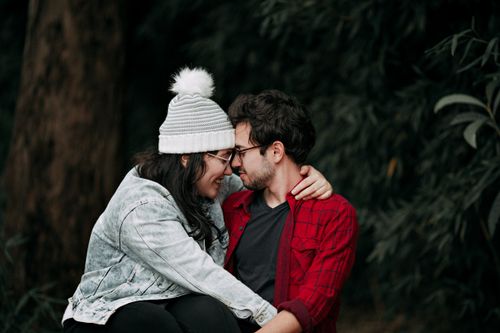 Free Young couple sitting closely, sharing affection outdoors in an autumn park, wearing casual attire. Stock Photo