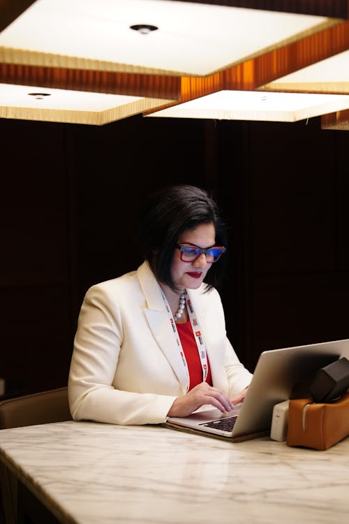 A woman in a white jacket and glasses using a laptop