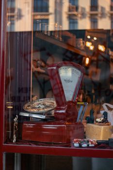 A vintage weighing scale showcased in an antique shop window with various delicacies and decor.