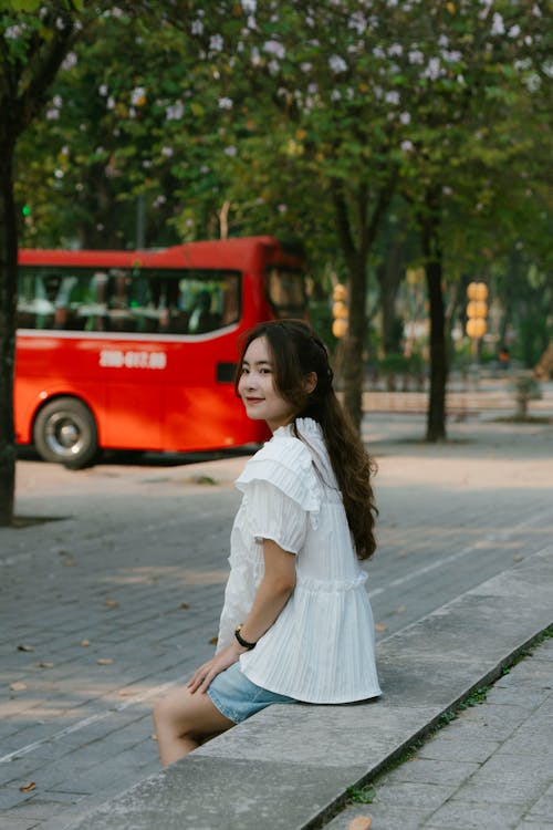 Free A woman sitting on a bench in front of a red bus Stock Photo