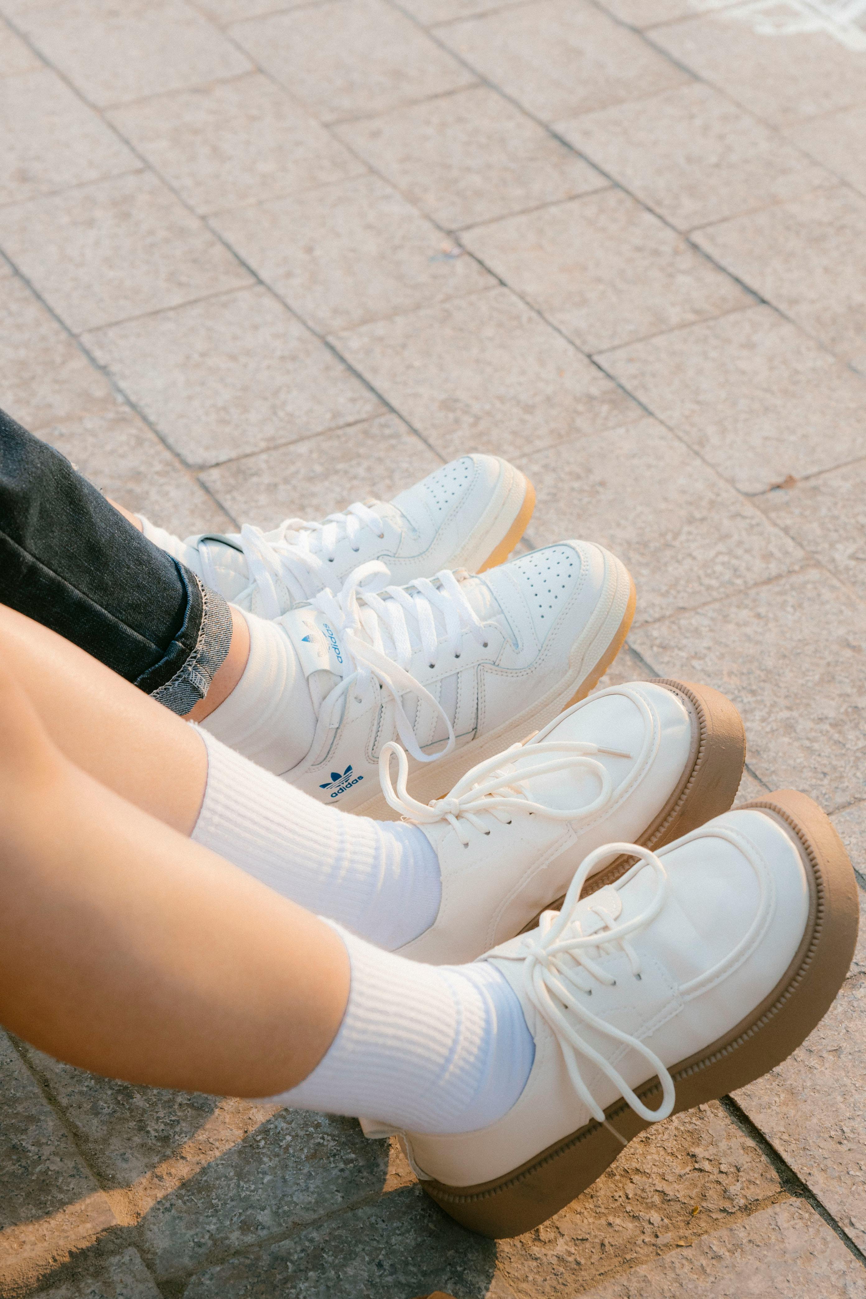 Two pairs of white sneakers on pavement, showcasing casual urban fashion style.