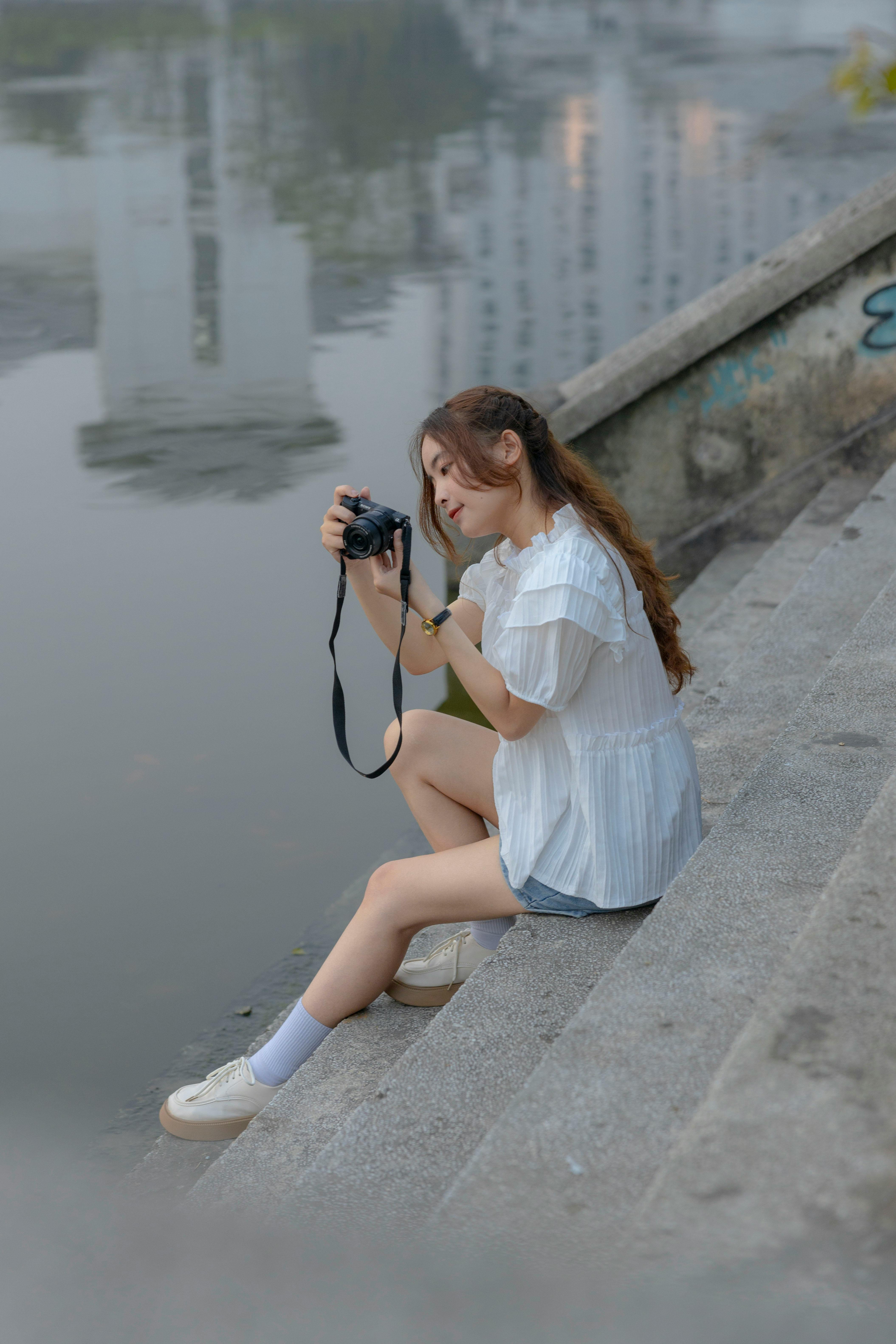 Young woman photographing by the serene canal, focusing on creative shots.