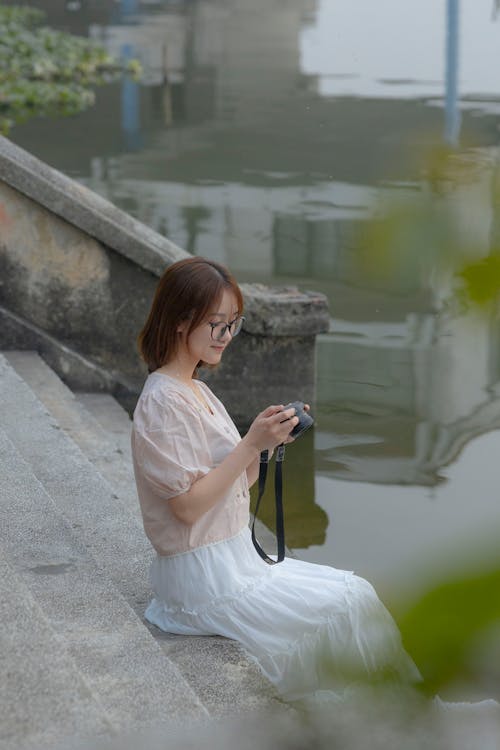 A woman sitting on the edge of a pond taking a picture