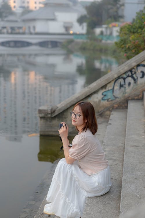 A woman sitting on the steps of a lake with a camera