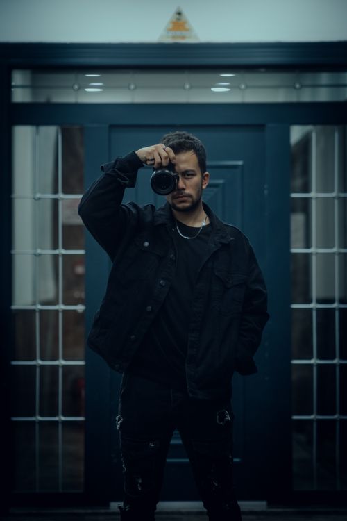 Free Stylish man in a black jacket taking self-portrait picture indoors with a camera. Stock Photo
