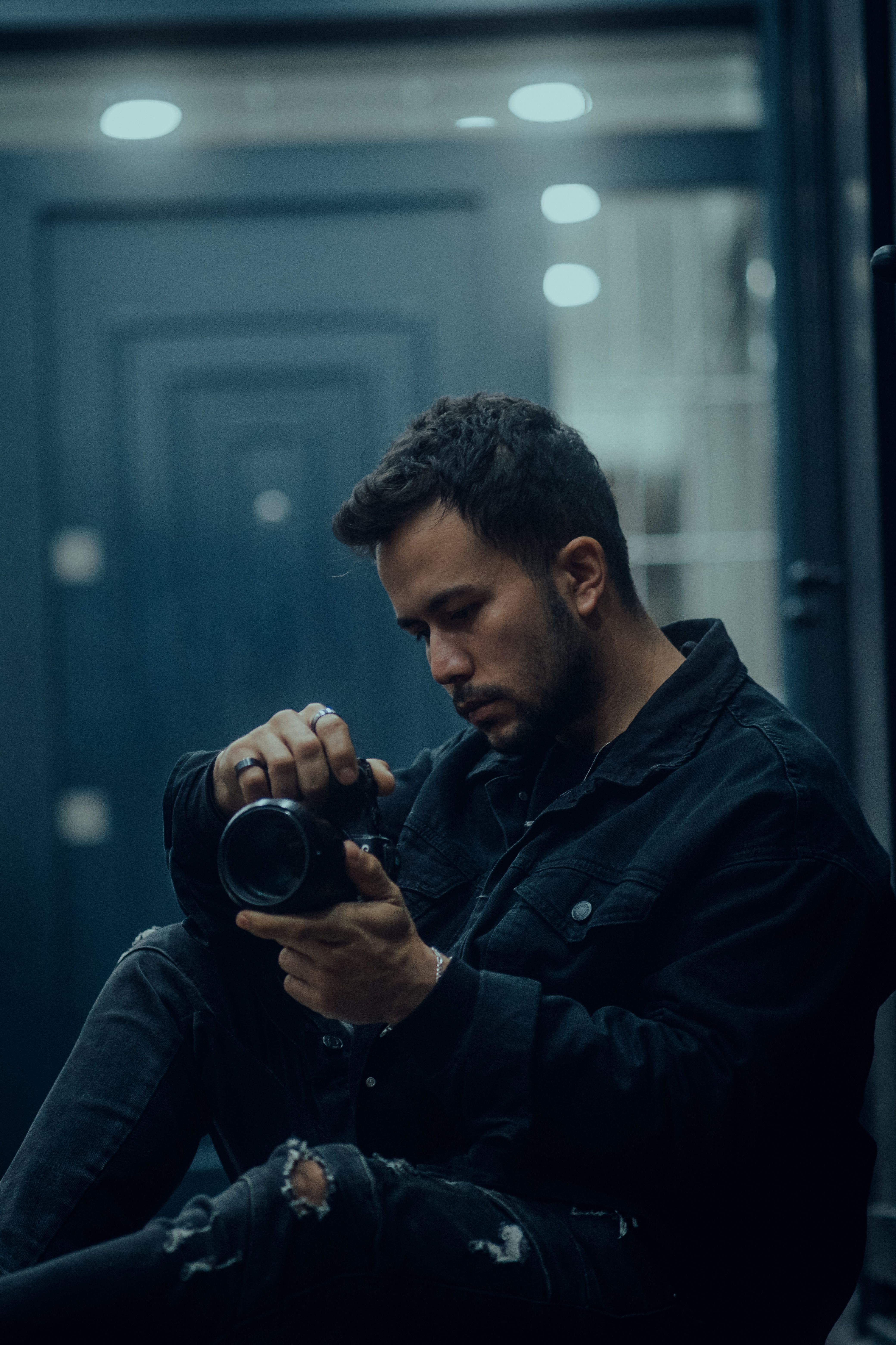 A young man reflects on his camera in a dimly lit urban environment, capturing a moment of introspection.