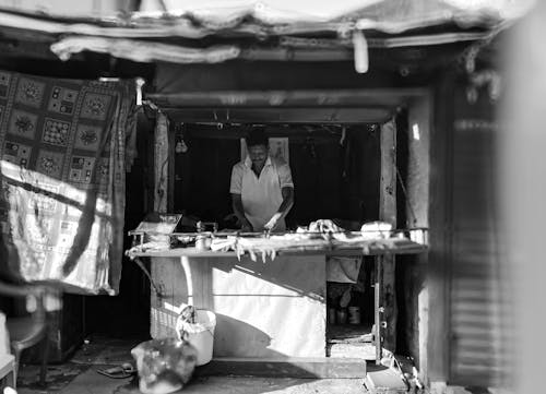 Black and White Photo of a Man Standing behind the Counter of a Market Stall 