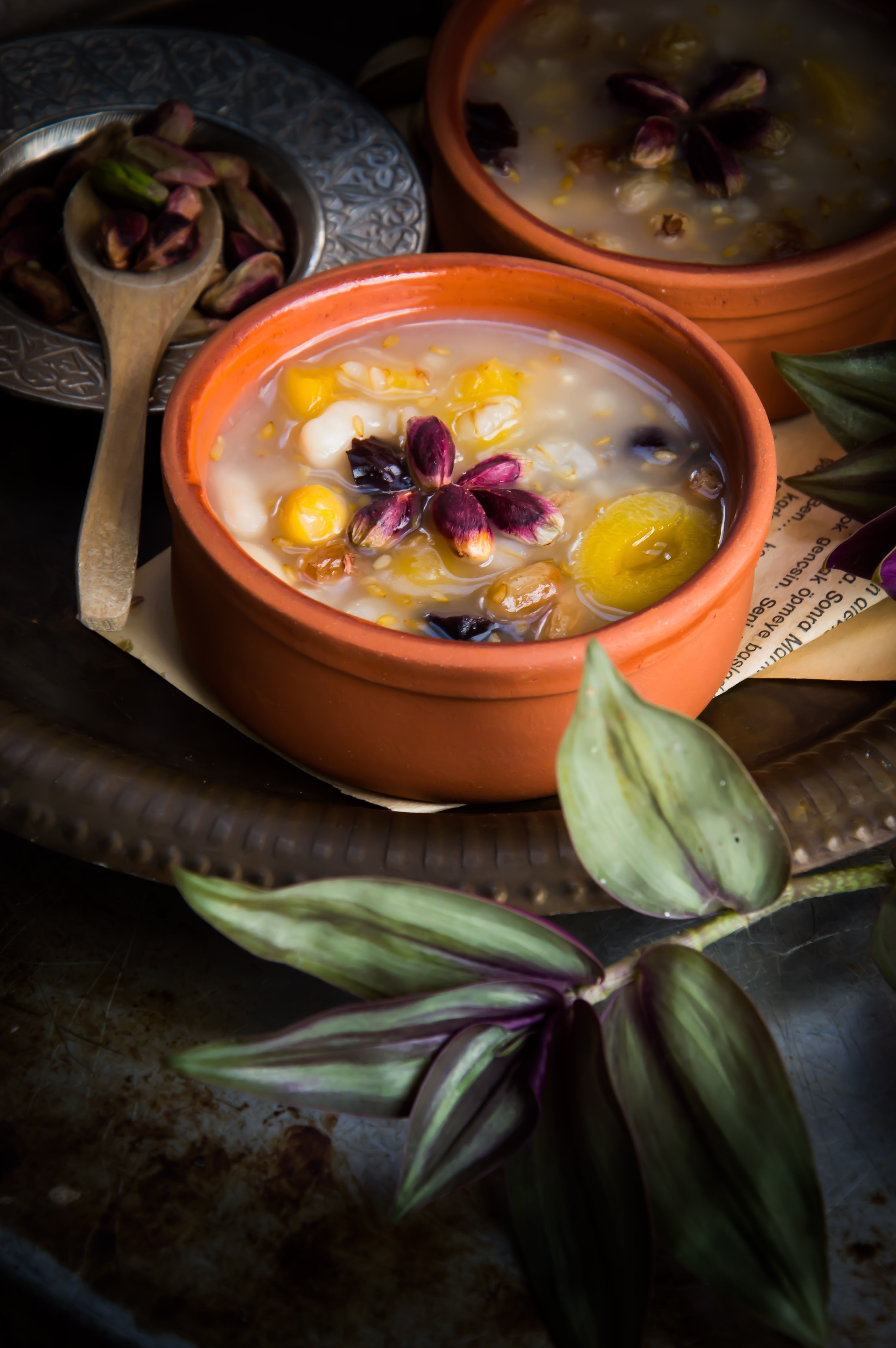 Close-up of gourmet soup with edible flowers in clay bowls on a rustic tray.
