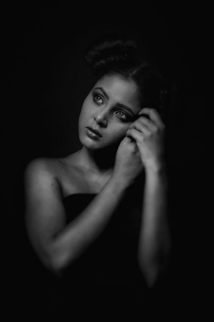 Elegant black and white portrait of a woman in deep thought on a dark background.