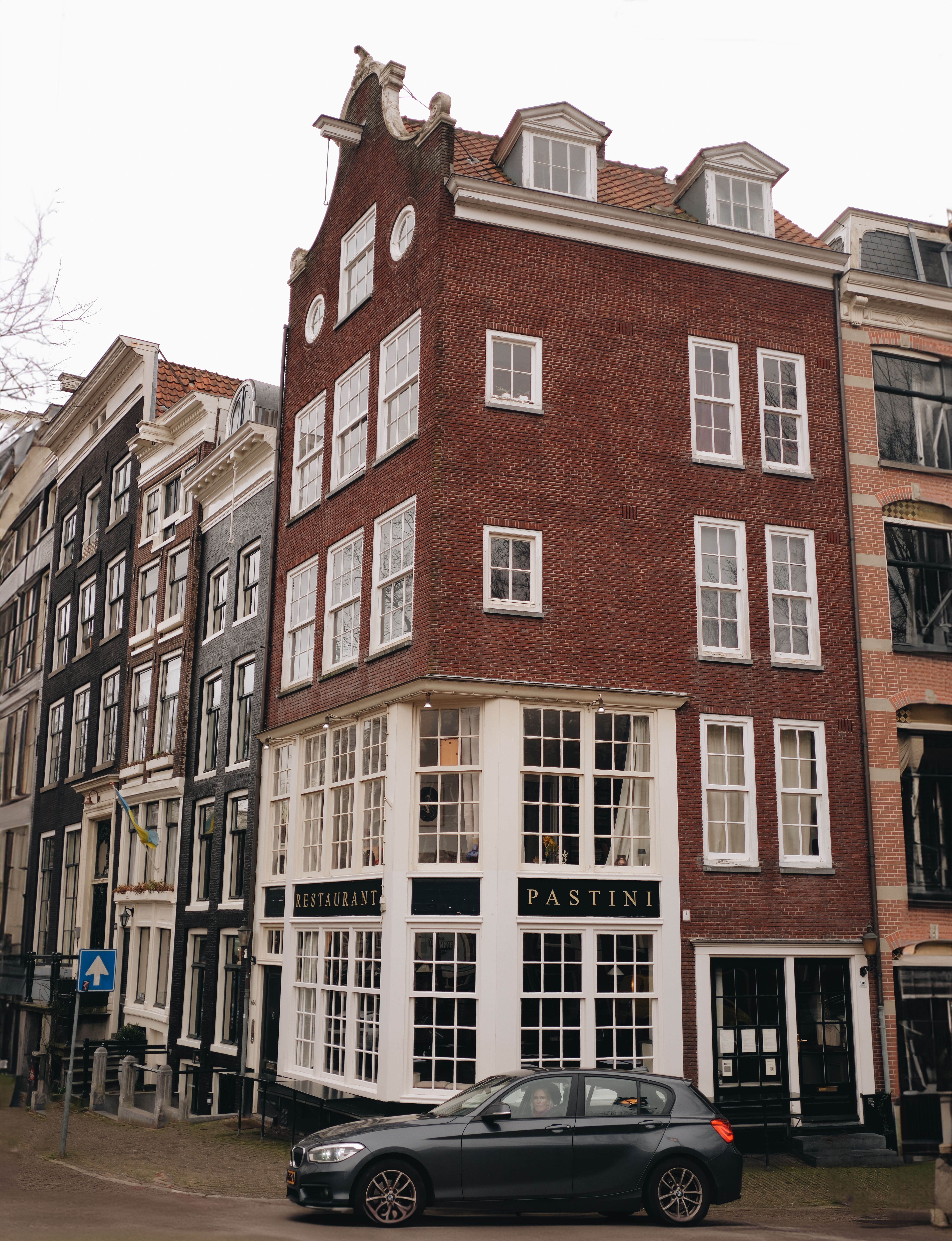 Charming street scene of a historic Amsterdam building with a restaurant at the corner with cars parked.