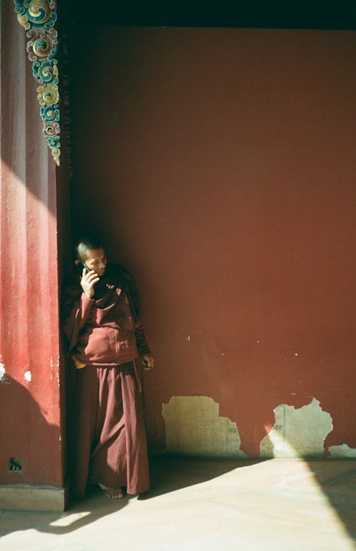 A monk in a red robe talking on a cell phone